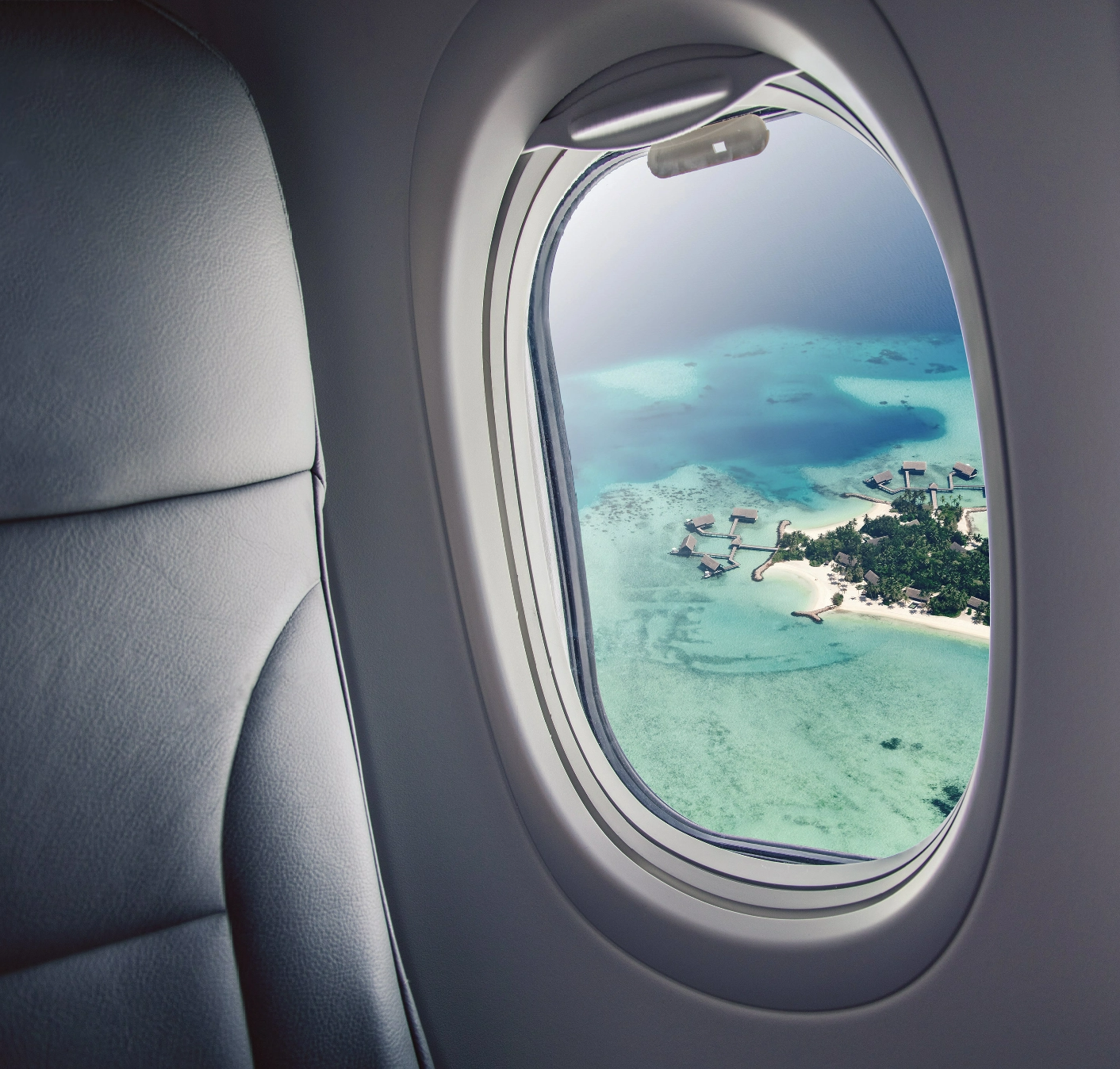 #BradescoAcessivel #ParaTodoMundoVer: a imagem é formada por uma janela de avião,
      com a vista para casas de bangalô em uma ilha paradisíaca, em meio a um mar com
      águas cristalinas.