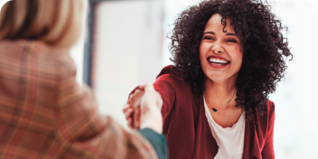 Duas mulheres apertando as mãos sorrindo, uma de frente e uma de costas